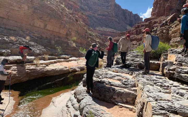 A group of students take a break from hiking near a stream in a canyon